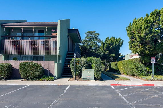 Front view of a two-story building with outdoor stairs and a wooden balcony.