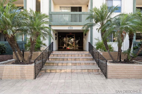 Front view of a multi-story building with a staircase entrance and palm trees.