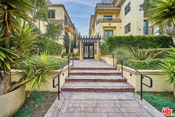 Front view of a multi-story residential building with steps leading to a gated entrance.