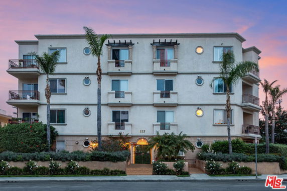 Front view of a multi-story apartment building with balconies and palm trees.