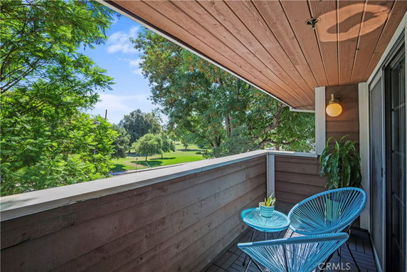 A small balcony with two chairs and a view of green parkland and trees.