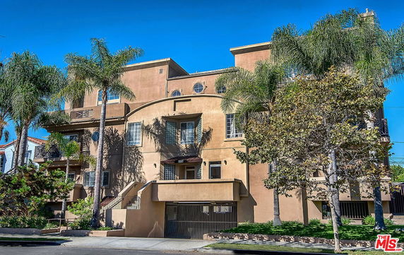 Front view of a multi-story residential building with balconies and palm trees.