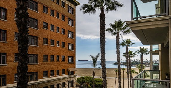 View from a building showing adjacent structures and a beach with palm trees.