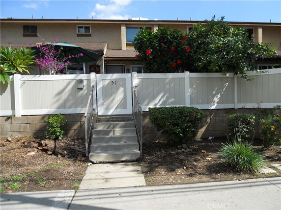 Front view of a house with a stairway leading to a gated entrance and a fenced yard.