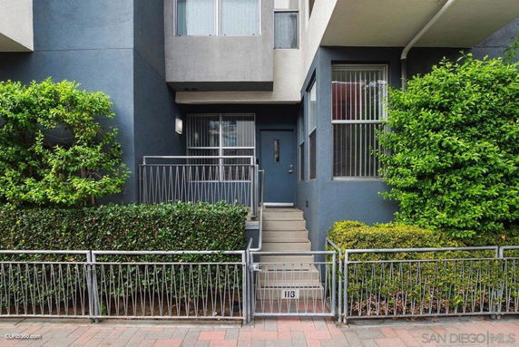 Front view of a modern multi-story building entrance with metal railings and greenery.