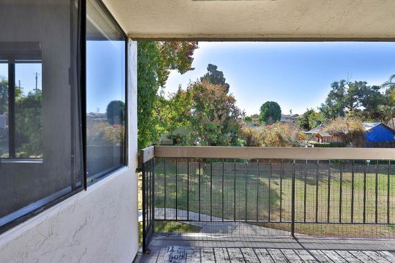 View from a balcony overlooking a grassy area with trees and adjacent buildings.