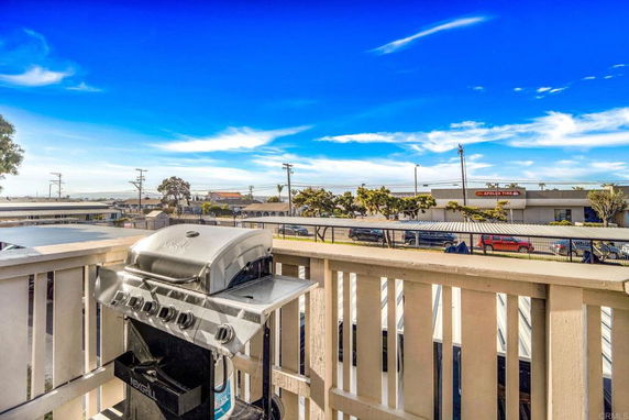 View from a balcony with a barbecue grill overlooking a street and nearby buildings.