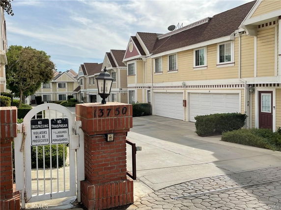 Front view of a row of two-story townhouses with garages and a gated entrance.
