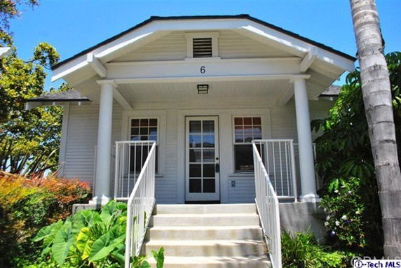 Front view of a small house with a covered porch and white railings.