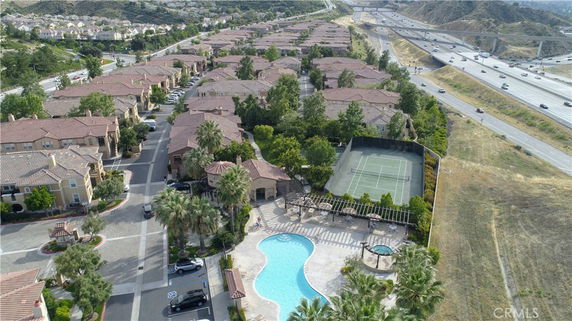Aerial view of a residential area with multiple houses, a swimming pool, tennis court, and nearby highway.