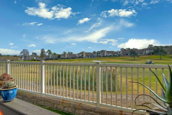 View from a fenced area overlooking a grassy field with houses in the distance.