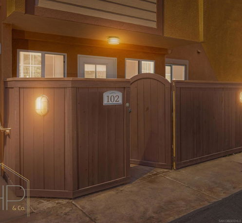Front view of a building entrance with a wooden gate marked 102 and exterior lighting.