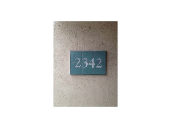 Exterior wall with a house number displayed on a plaque.