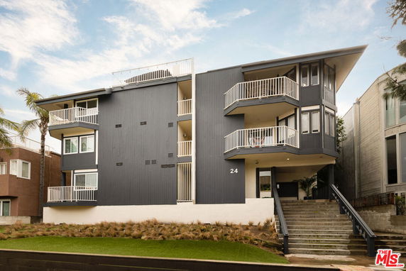 Front view of a multi-story apartment building with balconies and a sloped roof.