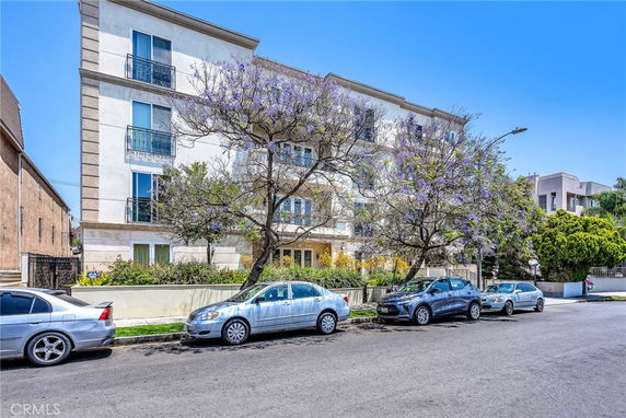 Front view of a multi-story building with balconies and cars parked in front.