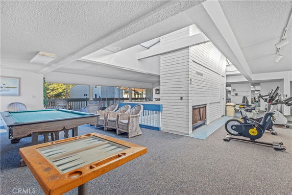 Interior of a club house with a pool table, wicker chairs, and gym equipment.