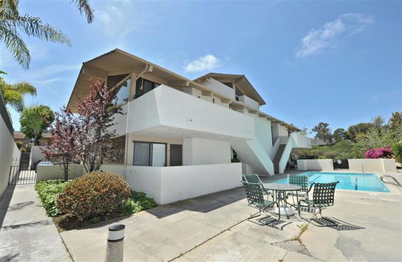 Front view of a two-story white building with exterior stairs and outdoor pool area.