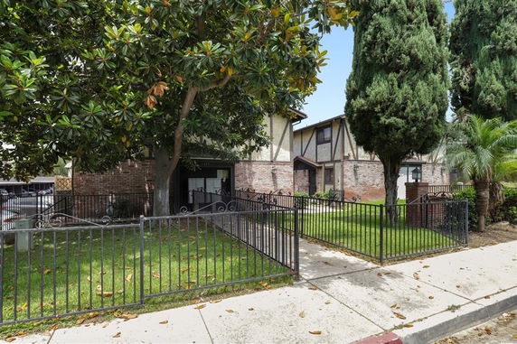 Front view of a two-story house with brick and stucco exterior, surrounded by trees and a metal fence.