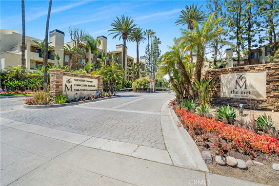 Front view of a multi-story residential complex with palm trees and landscaped entrance.