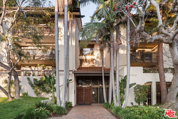 Front view of a multi-story residential building with balconies and lush landscaping.