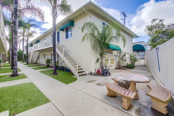 Front view of a two-story apartment building with exterior stairs and green awnings.