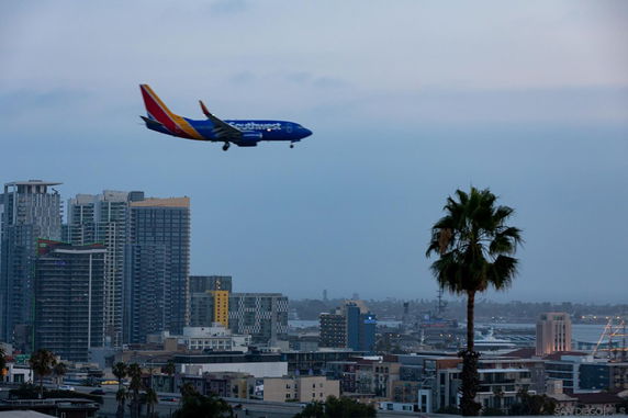 View of a cityscape with tall buildings and an airplane flying overhead.