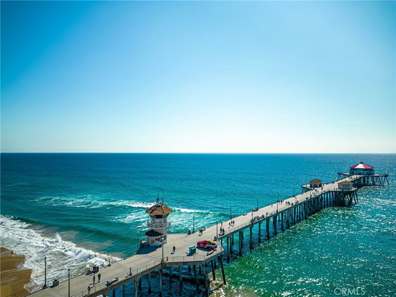 Panoramic view of an ocean pier extending over water with people walking and ocean waves surrounding.