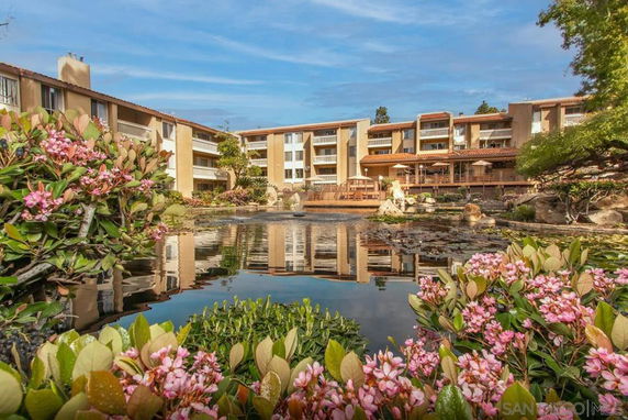 View of multi-story residential buildings with landscaped garden and pond.