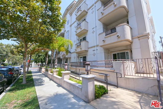 Front view of a multi-story residential building with balconies and a landscaped entrance area.