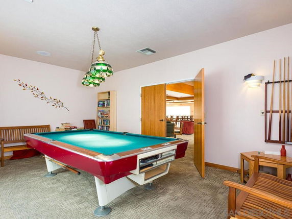 Room with a billiards table and seating area, featuring wooden furniture and decorative lighting.