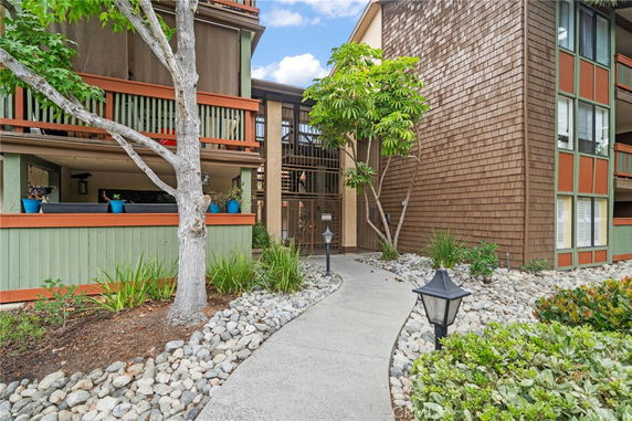 Front view of a multi-story residential building with wood paneling and a landscaped path.
