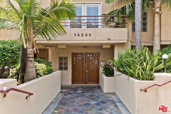 Front view of a building entrance with a wooden door and surrounding greenery.