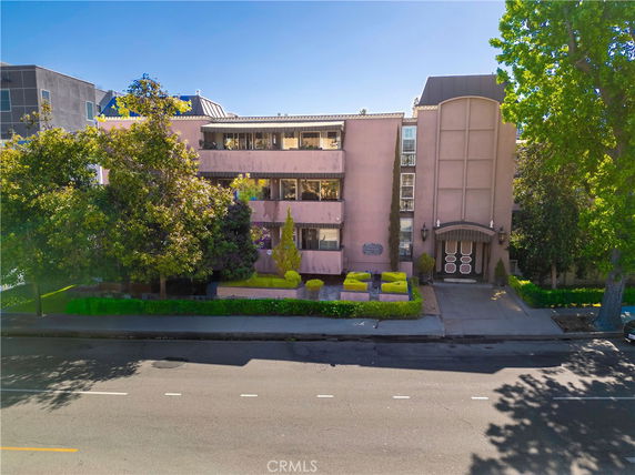 Front view of a multi-story building with trees and shrubs in front.