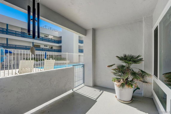 View of a swimming pool area with lounge chairs and an apartment building in the background.