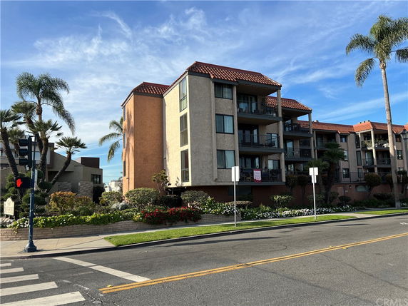 Front view of a multi-story apartment building with balconies and reddish-brown roof tiles.