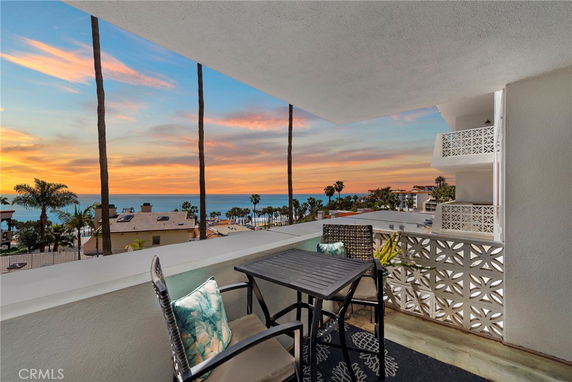 Balcony view overlooking ocean and sunset, with outdoor furniture.
