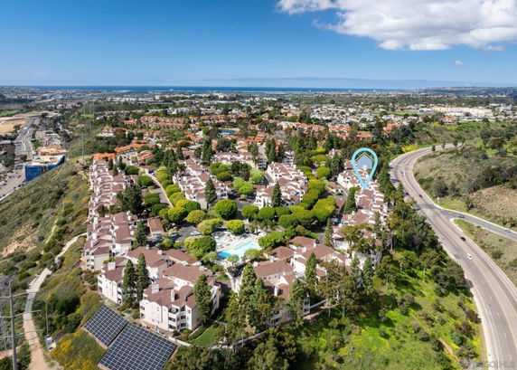 Aerial panoramic view of residential area with multiple buildings surrounded by greenery and nearby roads.