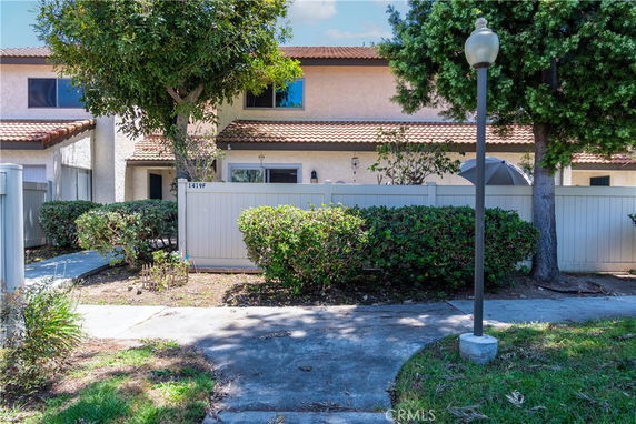 Front view of a two-story residential building with a tile roof and a small fenced yard.
