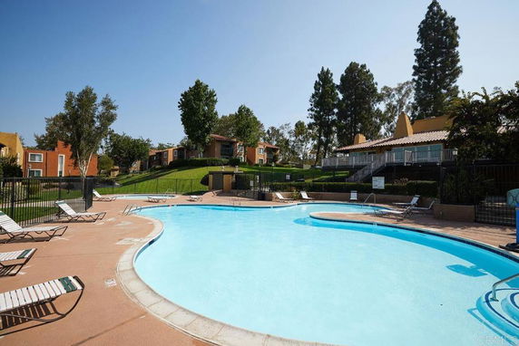 Outdoor swimming pool with surrounding lounge chairs and nearby residential buildings.
