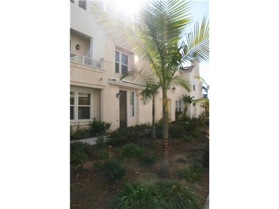 Front view of a multi-story residential building with balconies and windows, partially obscured by a palm tree.