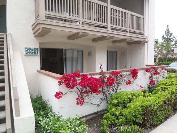 Front view of a multi-story building with a balcony and flowering shrubs.