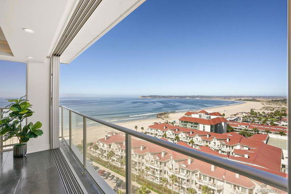 Wide angle view from a balcony overlooking the ocean and beach with buildings below.