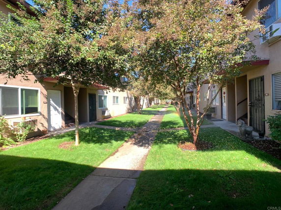 Front view of apartment buildings with multiple entrances and a central walkway lined with trees.