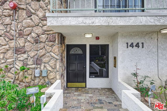 Front view of a building entrance with stone wall, black door, and the number 1441.