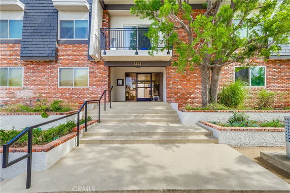 Front view of a multi-story brick building with an entrance staircase and a balcony.