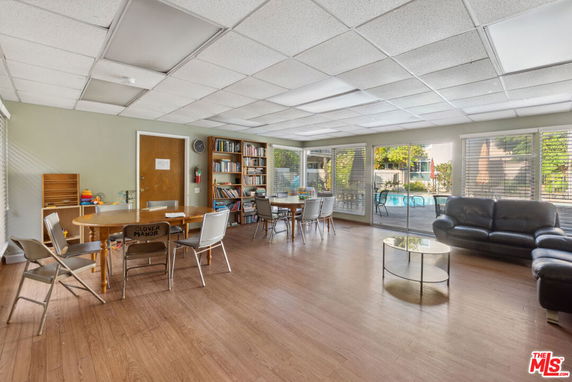Room with tables, chairs, bookshelf, and couches near large windows.