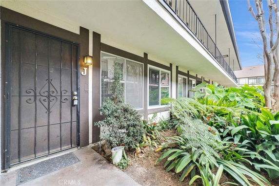 Front view of an apartment building with a secured entrance door and greenery.