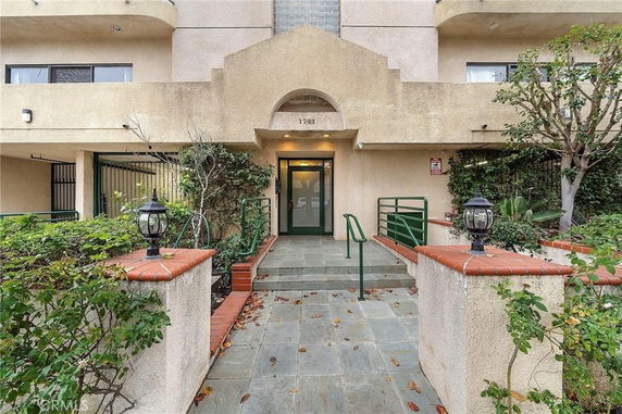 Front view of a multi-story building entrance with railings and plants.