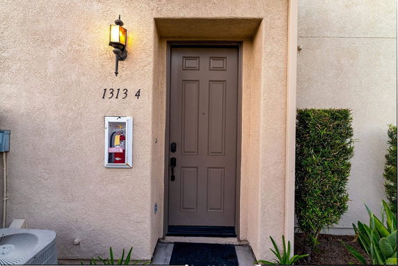 Front door of a house with an exterior light and a fire extinguisher mounted nearby.