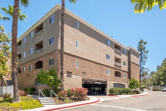 Front view of a multi-story apartment building with a parking area on the ground level.